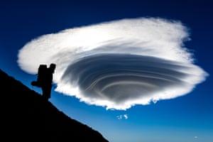 A hiker silhouetted against a blue sky with dramatic conical cloud
