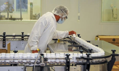 A lab technician in white coat and cap inspects drug bottles on a production line