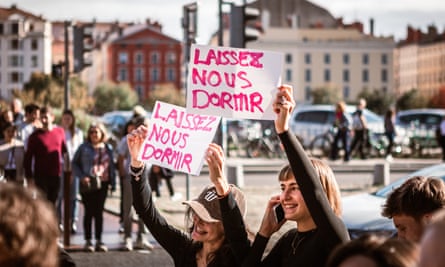 Two women, smiling, hold up signs that translate into English as ‘Let us sleep’ at a rally for Pelicot in Lyon