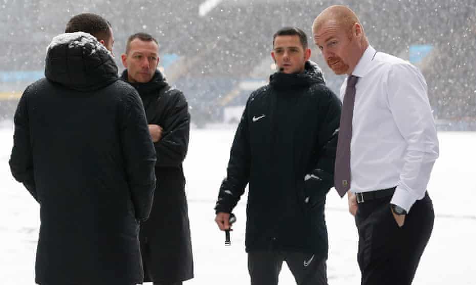 A jacket-less Sean Dyche braves the Turf Moor snow with match officials during a pitch inspection.