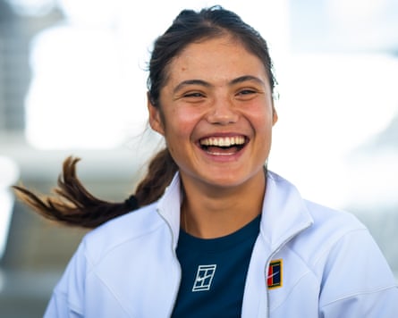 Emma Raducanu pictured from the shoulders up, smiling broadly as her hair plait swings behind