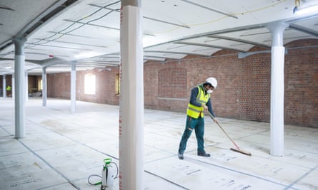 A site worker sweeps up in a room that was previously lined with service ducts and in which the original vaulted ceilings and brick walls were covered.