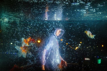 a child in a plastic poncho walks past dramatic fish in an ambiguously shot aquarium