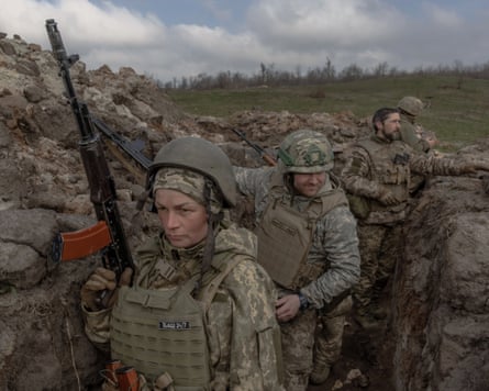 Soldiers in khaki, one of them holding a gun, in a trench