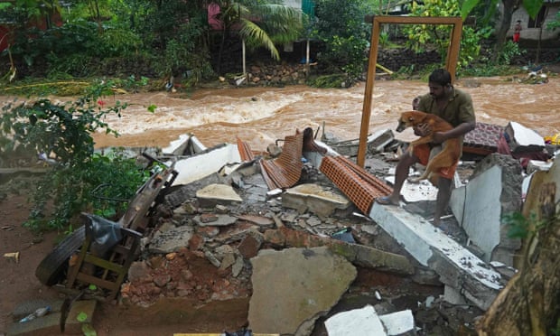 A Kerala resident carries a dog amid the debris of his home after flash floods hit.