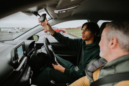 A driving instructor shows a young male student how to adjust his rear view mirror during a driving lesson