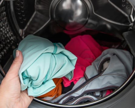 A person loading sportswear into a washing machine.