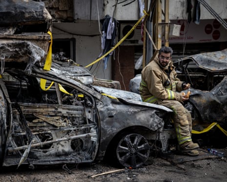 A firefighter takes a break on a vehicle destroyed on in an Israeli airstrike in Lebanon