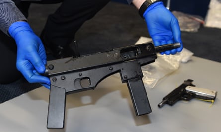 Blue-gloved police display a homemade submachine gun seized in 2016. A pistol is also lying on the floor.