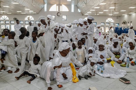 A large group of women and young children, all dressed in white, gather in a church building