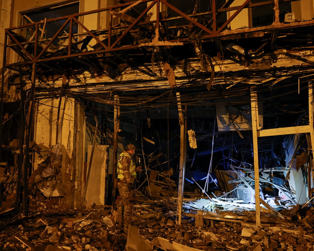 A police officer inspects a dark, debris-strewn building damaged by a missile strike