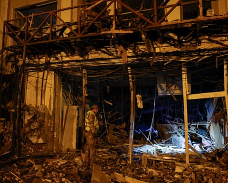 A police officer inspects a dark, debris-strewn building damaged by a missile strike