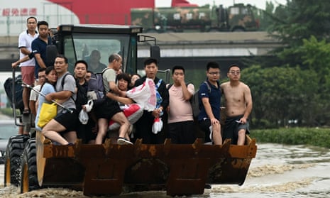People ride in the front of a loader to cross a flooded street in Zhengzhou, Henan province