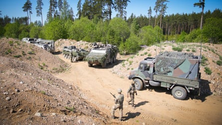 Troops and vehicles on a dusty dirt road on the edge of a forest