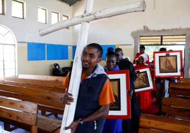 Image 24: A Christian carries a wooden cross while others follow carrying crucifixion paintings