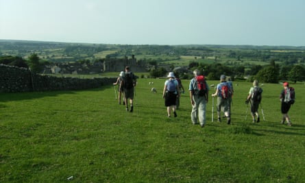 Ramblers walking across lush green fields towards a ruined Castle