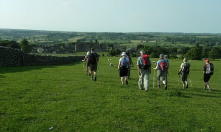 You'll never walk alone: 10 great UK walking festivals for spring and summer | walking holidays 6 Ramblers walking across lush green fields towards a ruined Castle