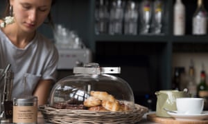 Waitress behind the counter at Bistro Lotte, Frome, Somerset, UK. On the counter are pastries and coffee cups.