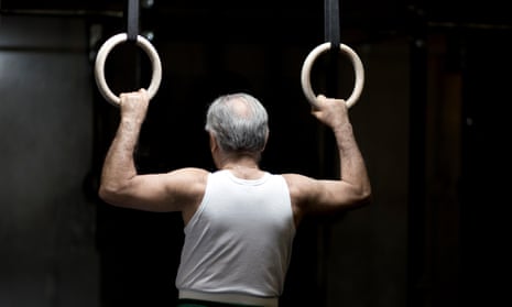 Rear view of senior man holding gym rings in dark gym