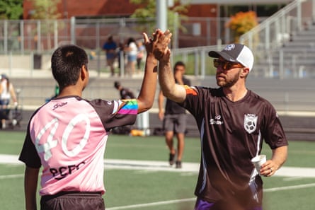 a man in a black jersey high-fives a young soccer player with dark hair on a field