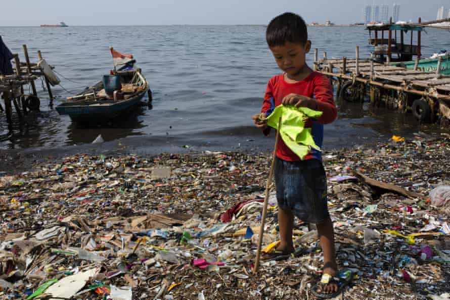 A boy plays with a makeshift flagpole on a beach covered in plastic waste in Indonesia.