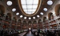Interior of the French national library. Books line the walls and there are desks with lamps across the room.