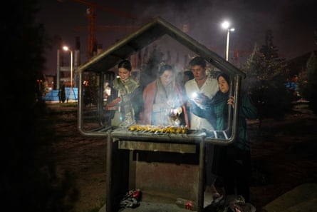 Four people stand at a covered outdoor grill.
