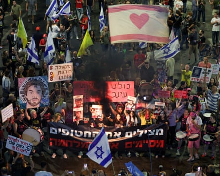 a large crowd of people hold banners and flags in a street at night