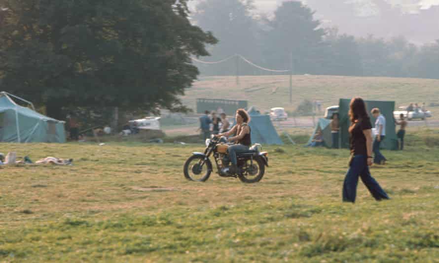 Michael Lang riding on his motorcycle through the camping area as people put up tents in August 1969.