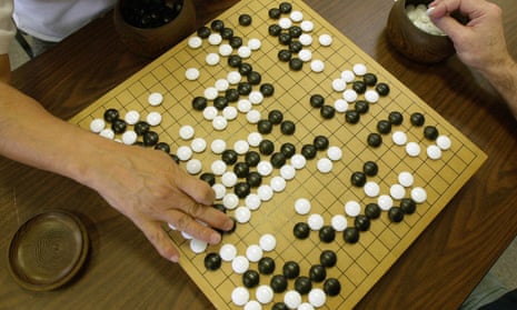 A player places a black stone while his opponent waits to place a white one as they play Go, a game of strategy.