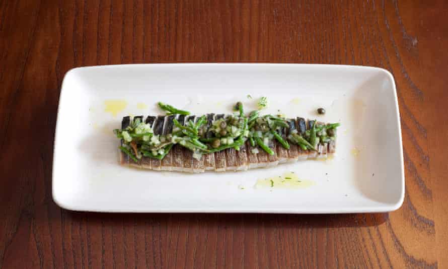 An oblong plate of mackerel tightly sliced and sprinkled with cucumber and capers