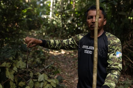 An Indigenous man stands in the jungle holding a snake