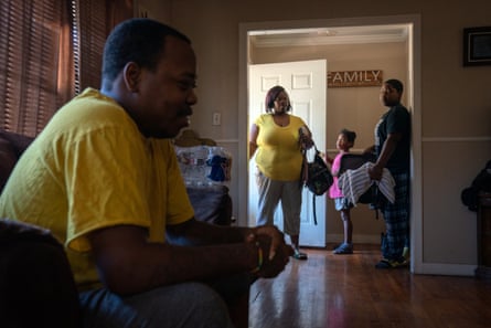 Three people at the entrance of a house, a man sitting on the couch in the foreground