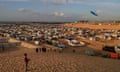 A Palestinian boy flies a kite on the sand in Rafah, with hundreds of tents in the background