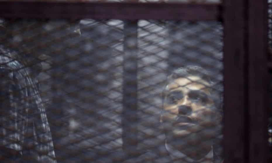 Baher Mohamed, left, and Mohamed Fahmy listen to their verdict in a soundproof cage in a courtroom in Tora prison in Cairo. Their initial 2014 conviction said the journalists had been brought together ‘by the devil’ to destabilise Egypt. 
