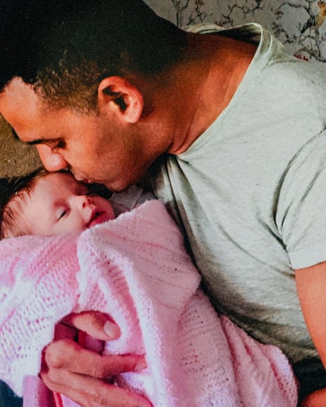 A man holding a baby wrapped in a pink blanket and kissing her on the forehead
