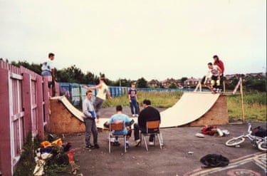 A group of people sitting around a skateboarding ramp, while others are skating