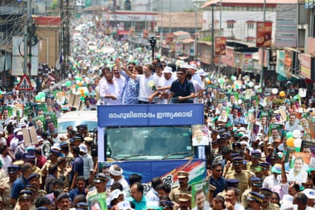Crowds gather around an open-top bus as Gandhi waves to them