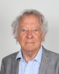 An older white man in a suit jacket and open-necked shirt