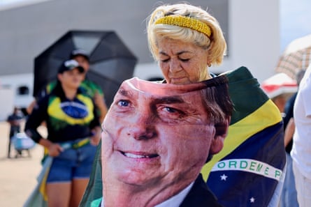 An elderly woman shuts her eyes as she wraps herself in a flag with Bolsonaro’s face on it