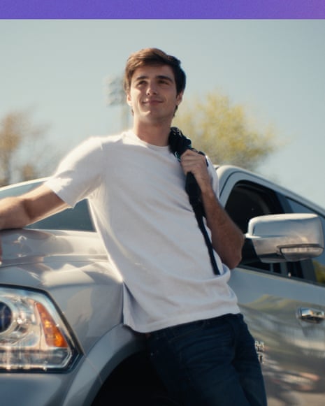 Jacob Elordi as Nate in series one of the tv show Euphoria. He leans against the bonnet of a car, wearing a white T-shirt.