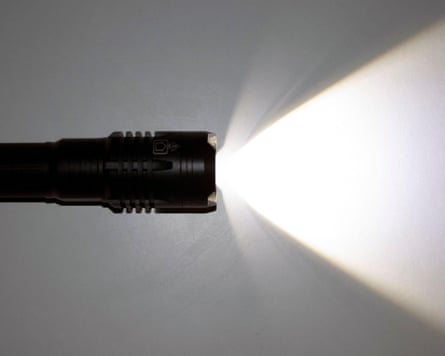 A black torch lies on a grey surface, projecting a bright beam of light sideways
