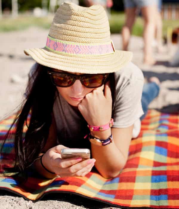 Woman texts on a mobile phone while lying on a picnic blanket