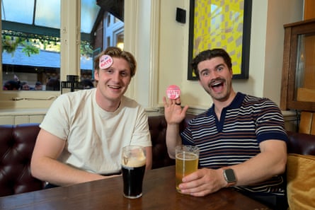 Two men sit in a pub with drinks on the table in front of them