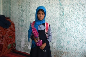A solemn-looking girl in a blue hijab stares at the camera