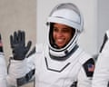 Woman in astronaut suit and helmet waves and smiles.