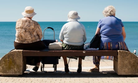 A rear view of three old elderly women sitting on a seaside bench