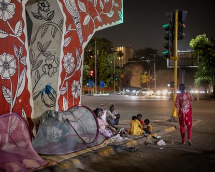 A group of people sit on the pavement next to two mosquito-netting tents