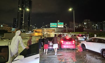People wade through a submerged street after heavy rain in the United Arab Emirates