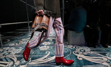 A model (pictured from waist down) wears patent red cowboy boots under pink and blue pyjama trousers, and carries a brown leather satchel-style bag